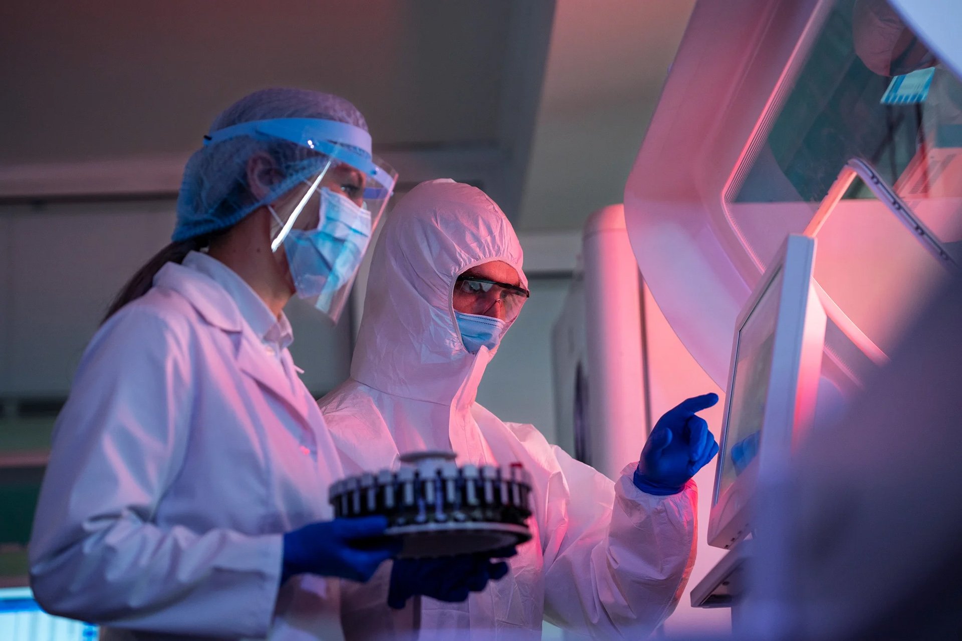 Scientists in protective gear operating a touchscreen machine in a laboratory with specialized equipment.