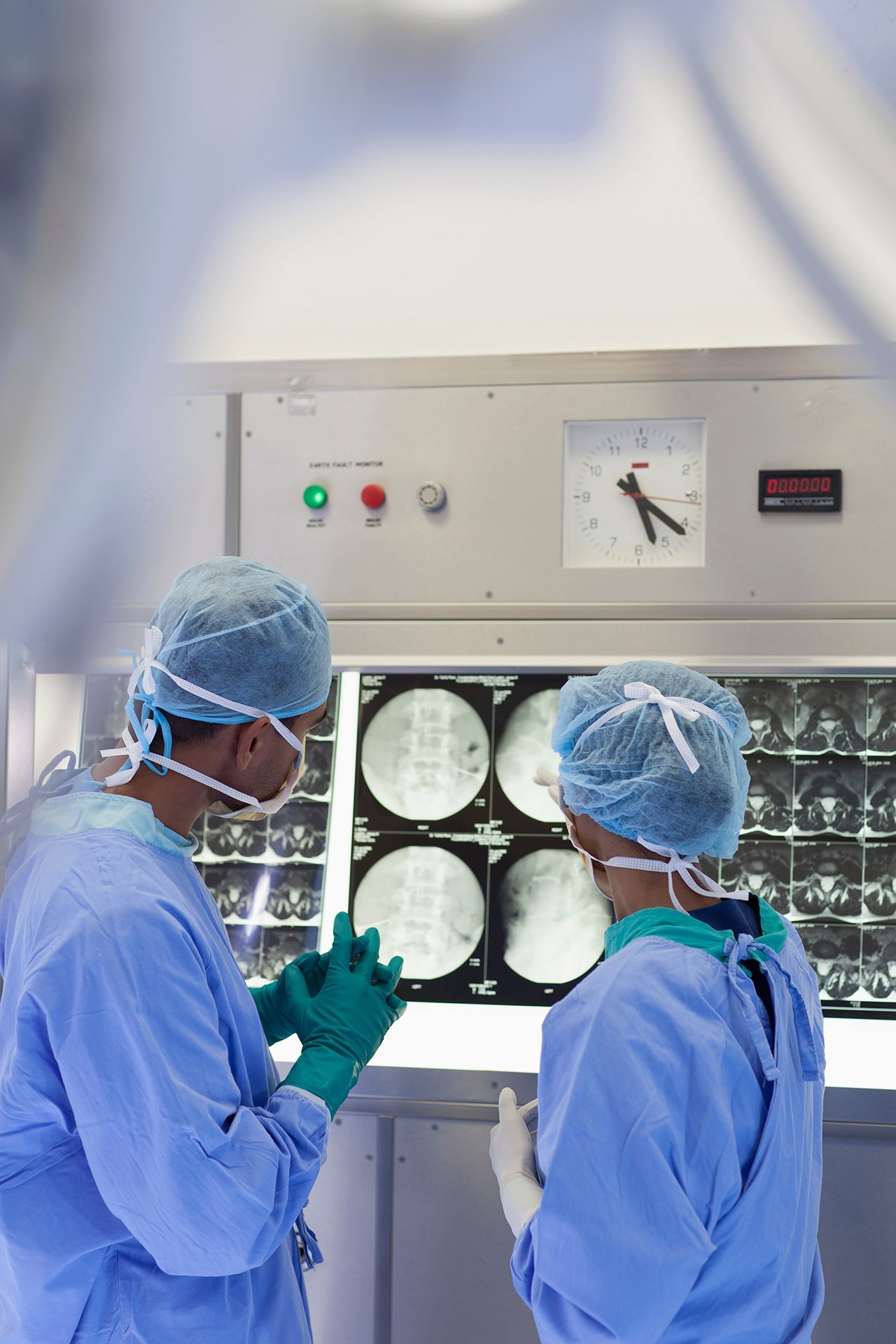 Two surgeons reviewing spinal X-ray images on a lightbox in an operating room.