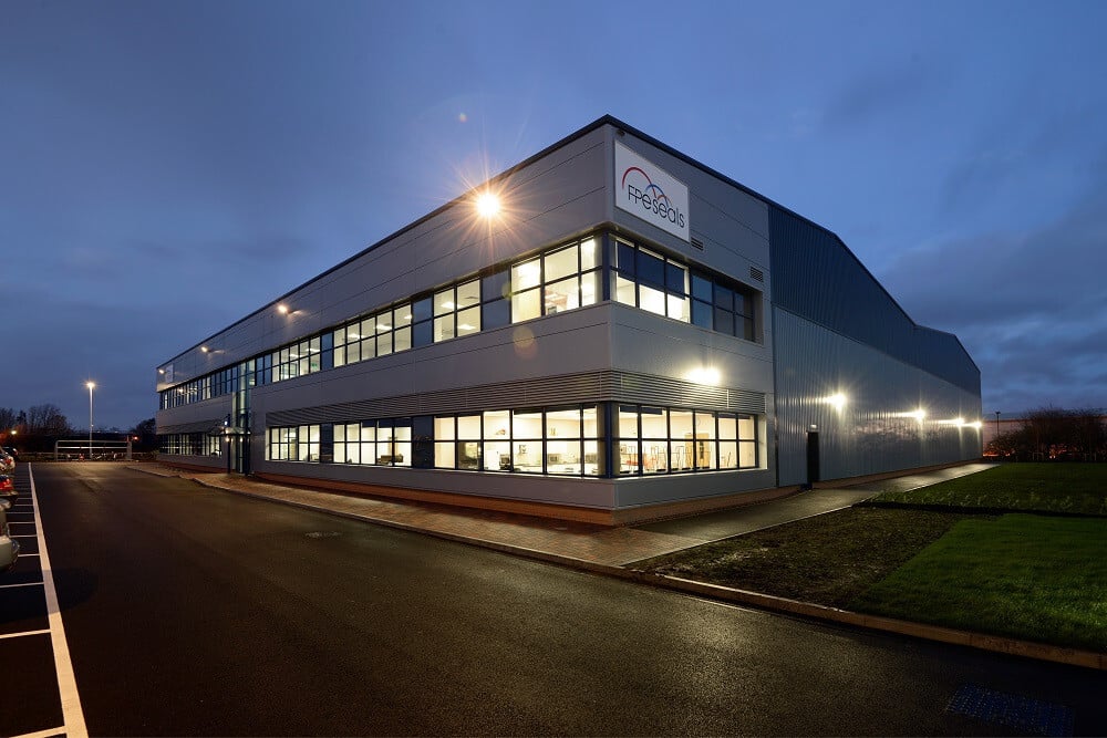 Modern industrial building of FPS Seals illuminated at dusk with parking lot and lights.