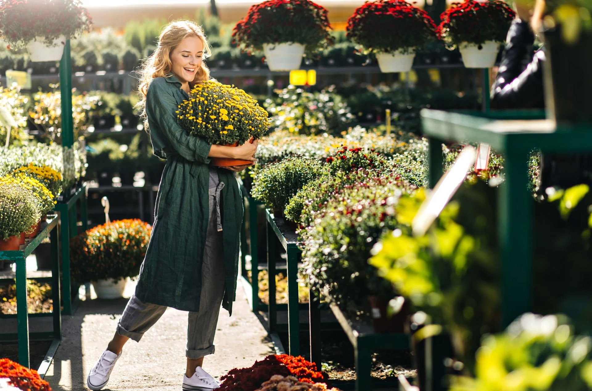 Woman holding a pot of yellow flowers while shopping in an outdoor garden center.