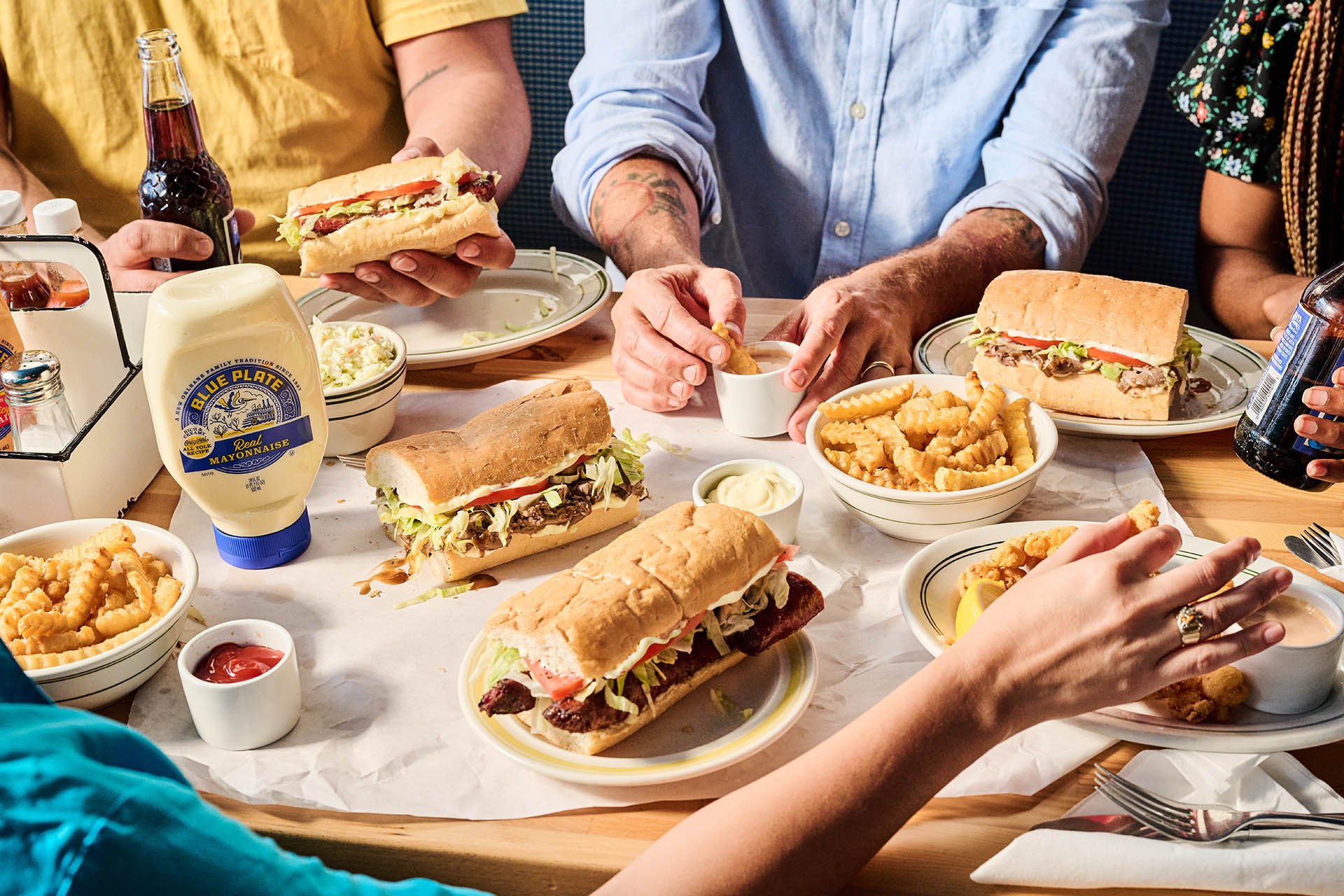 Group of people sharing a meal with sandwiches, fries, and Blue Plate mayonnaise at a restaurant table.
