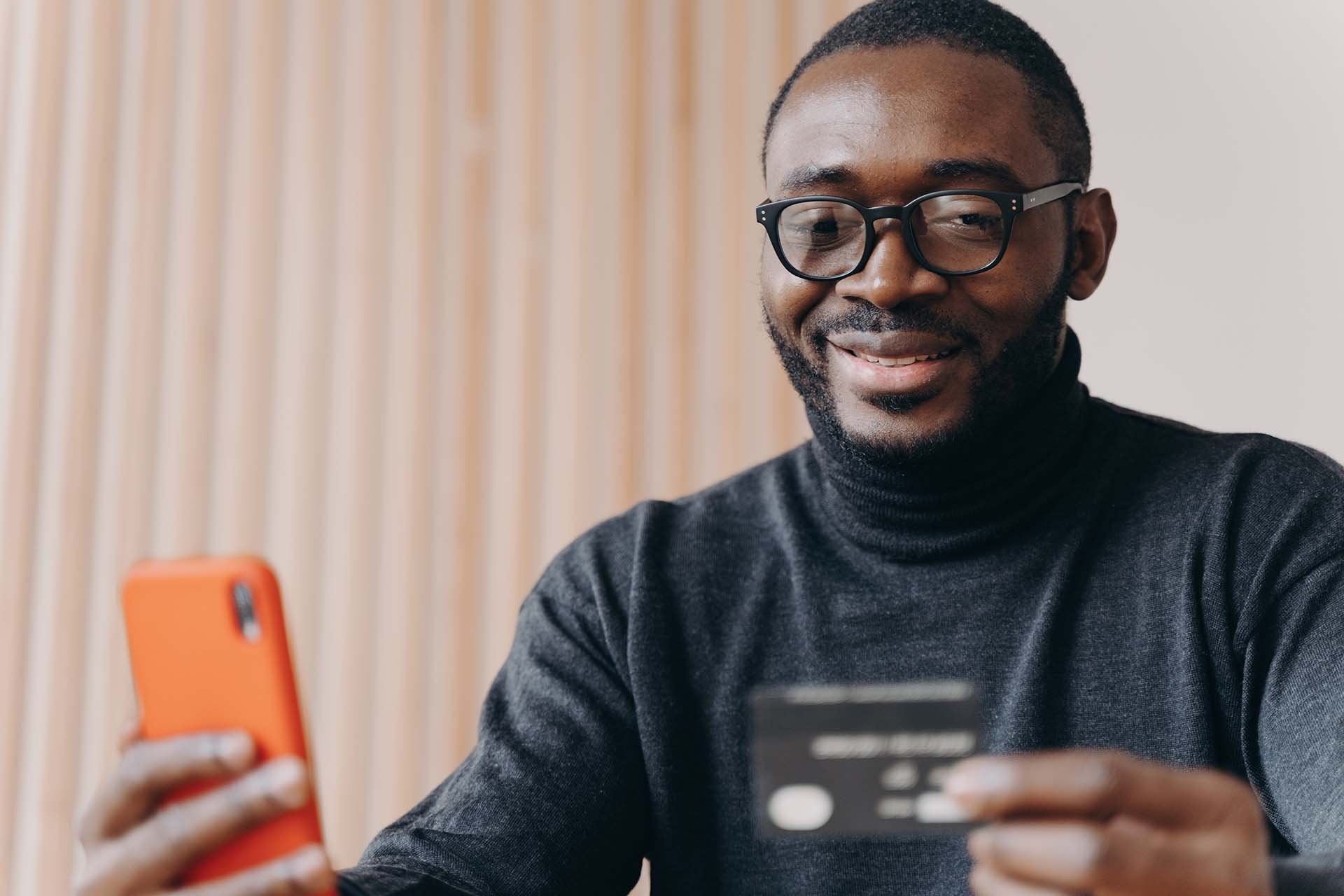 Smiling man holding a smartphone and credit card for an online transaction.