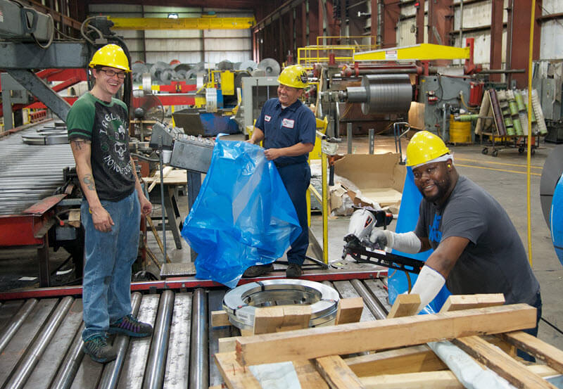Group of factory workers in safety gear working with industrial machinery and materials.