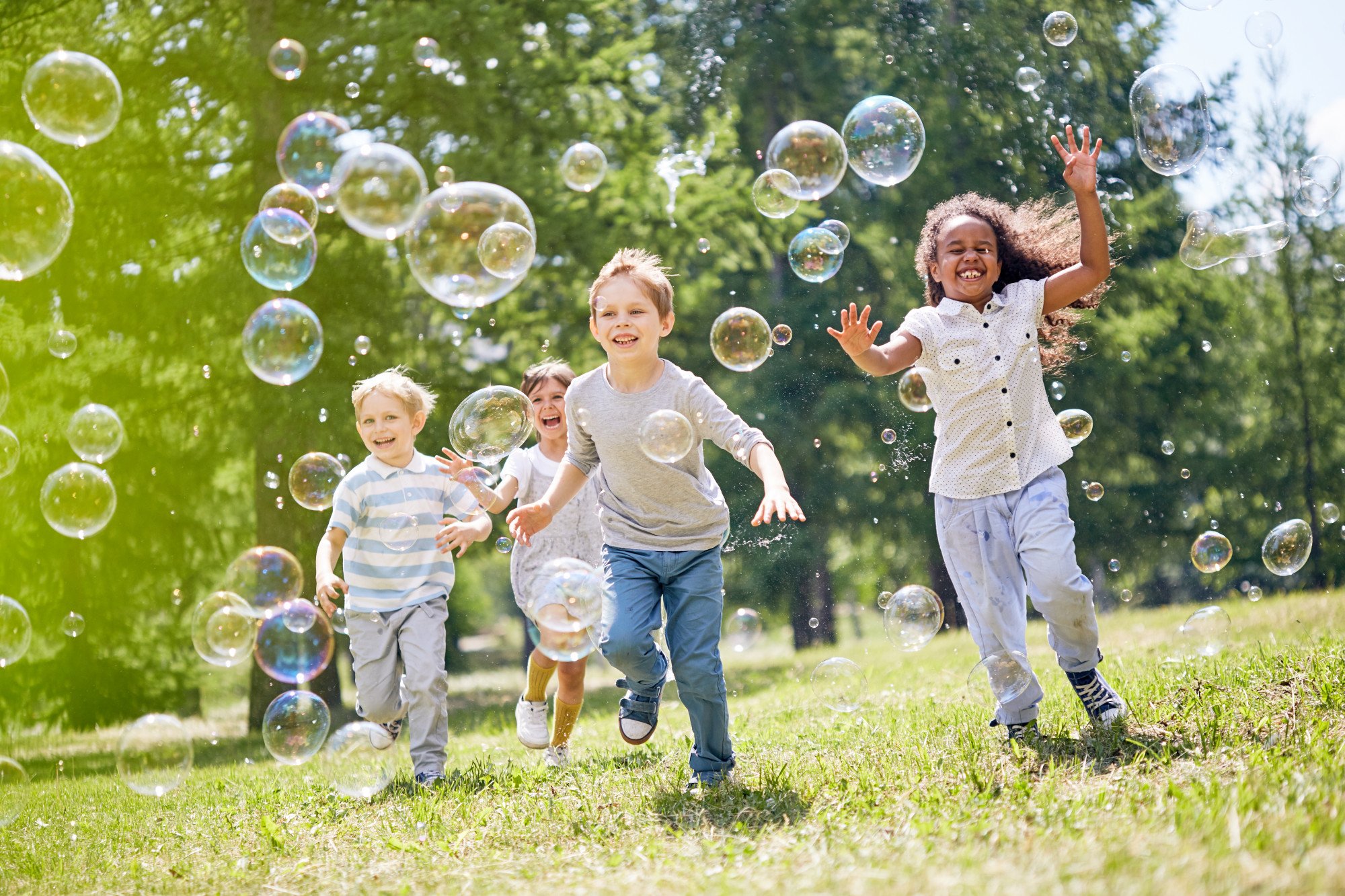 Group of children running and playing with bubbles in a grassy park.