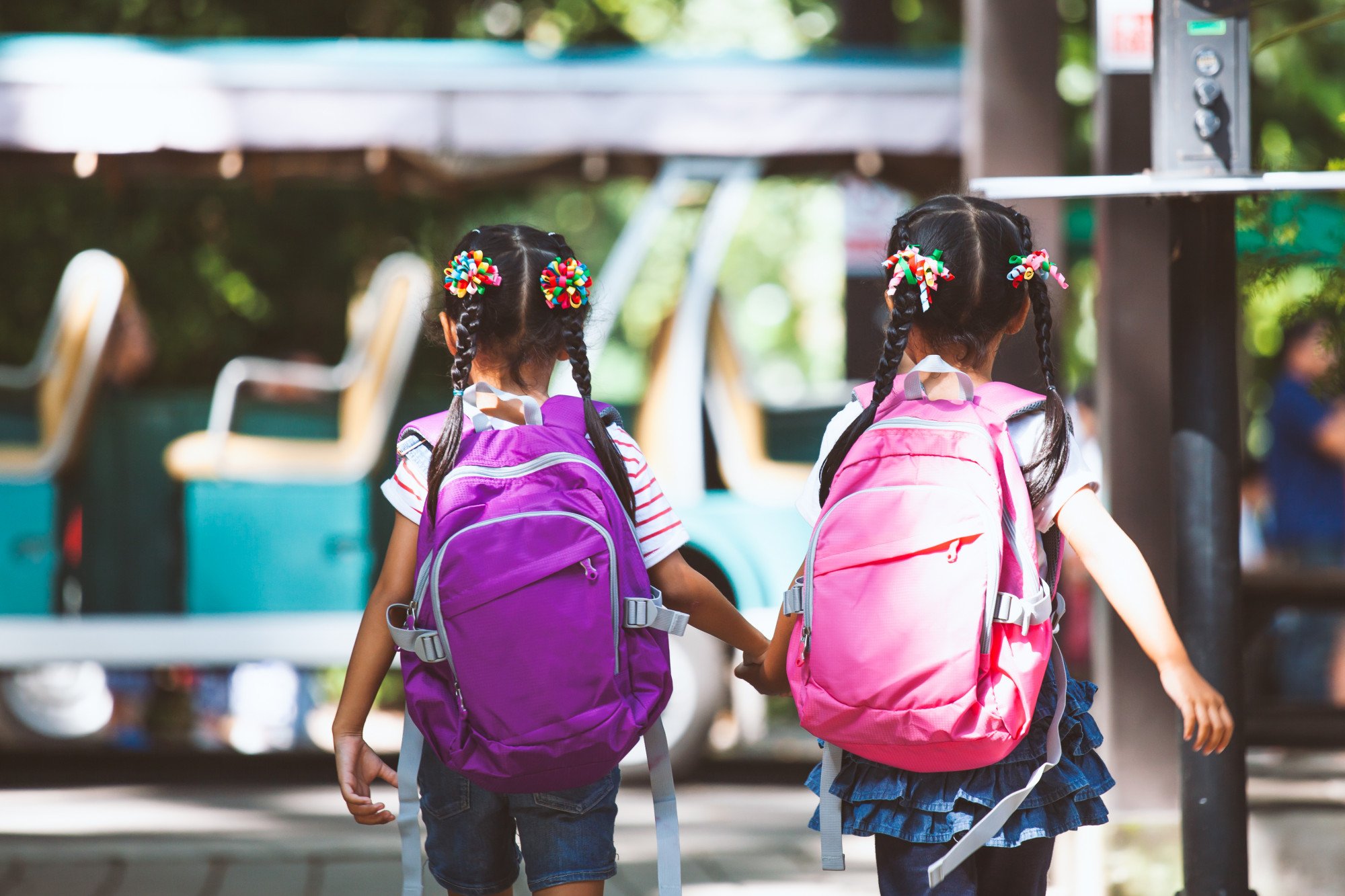 Two young girls wearing backpacks, holding hands while walking outdoors.