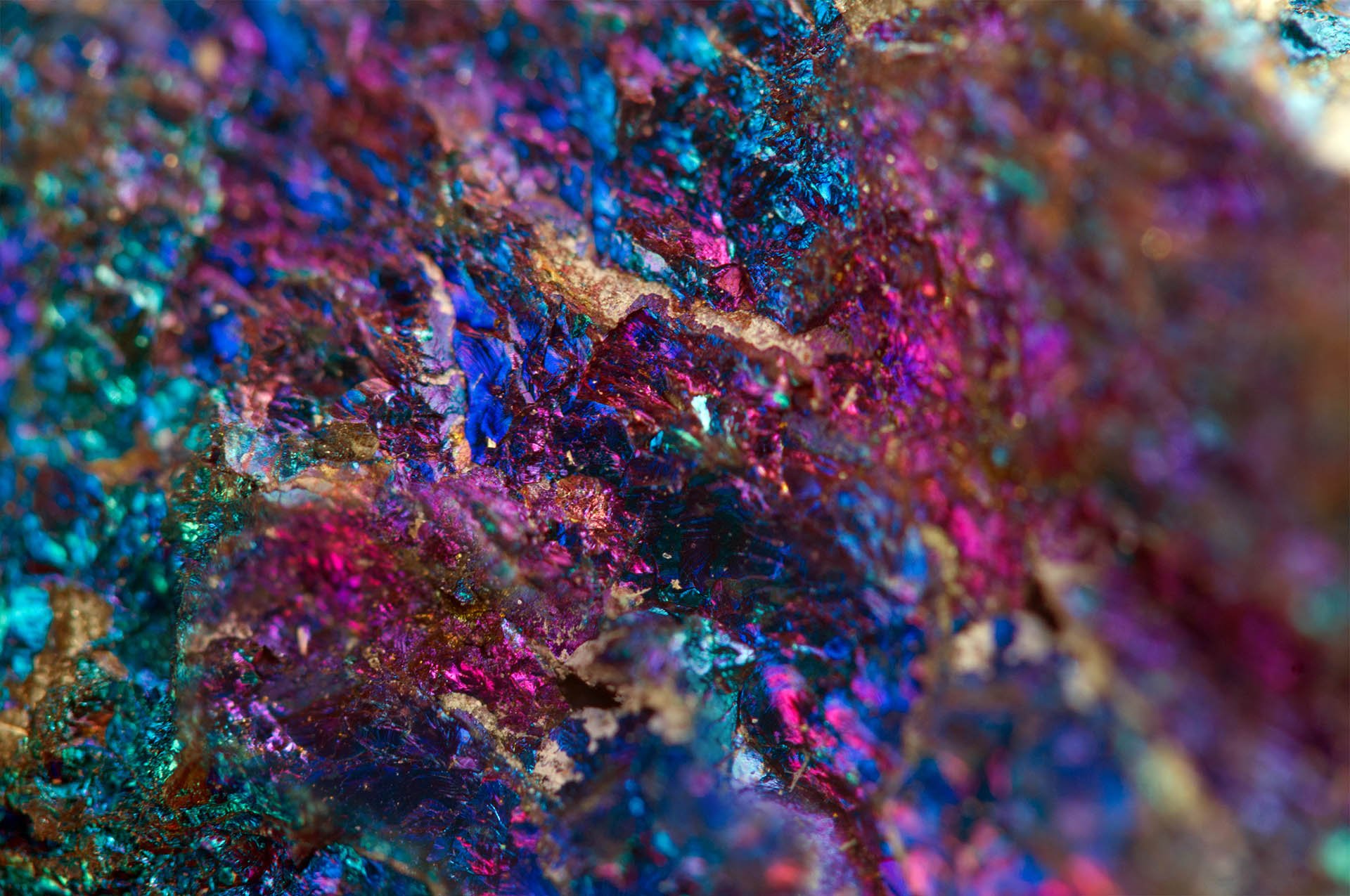 A vibrant, multicolored mineral surface showcasing rich shades of blue, purple, and gold with shimmering, crystalline textures.