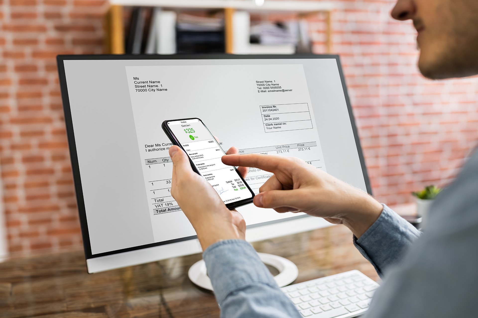 A person reviews an invoice on a computer screen while checking details on their smartphone, indicating digital document management.