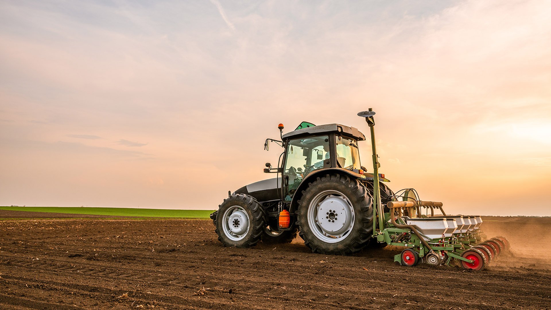 A modern tractor plowing fields at sunset, with a clear sky and vibrant colors, showcasing agricultural productivity.
