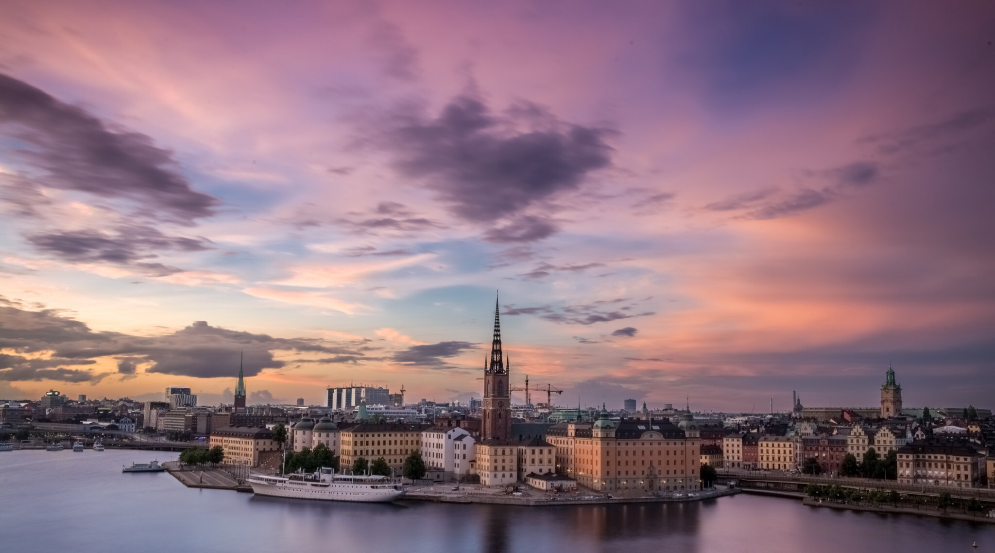 Cityscape of Stockholm at sunset with colorful sky, historic buildings, and waterfront reflections.