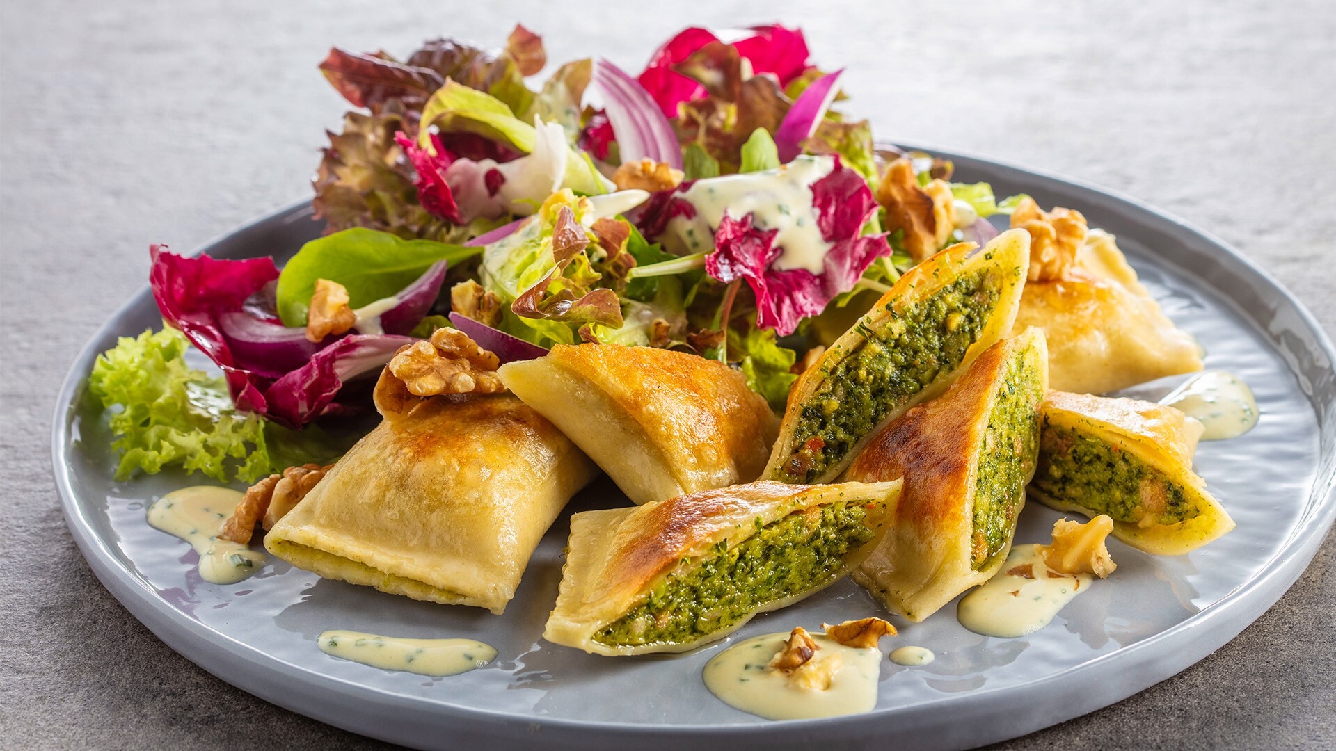 Plate of stuffed pasta with green filling, served with mixed salad, walnuts, and creamy dressing.