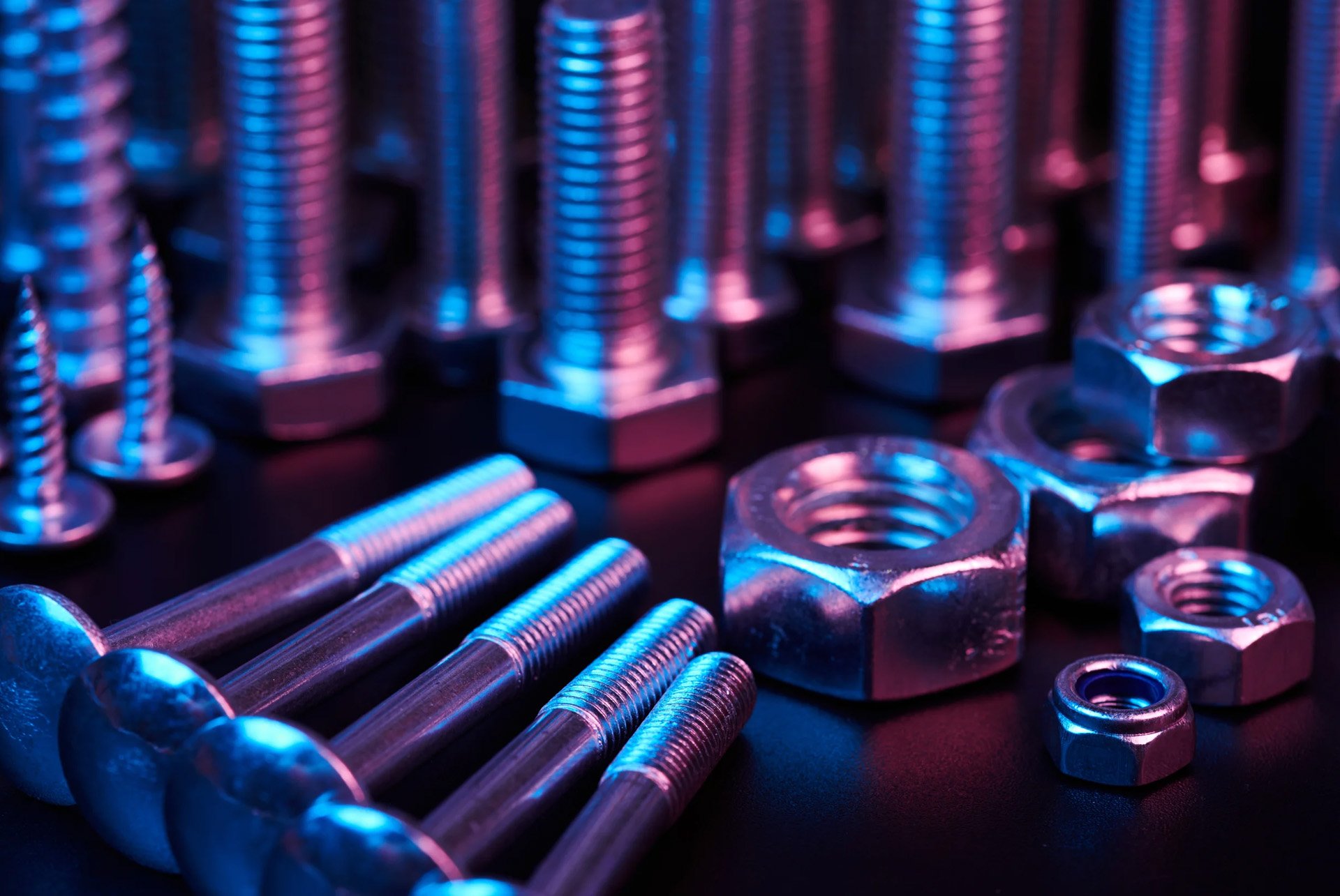 Close-up of metallic bolts and nuts with blue and pink lighting on a dark surface.