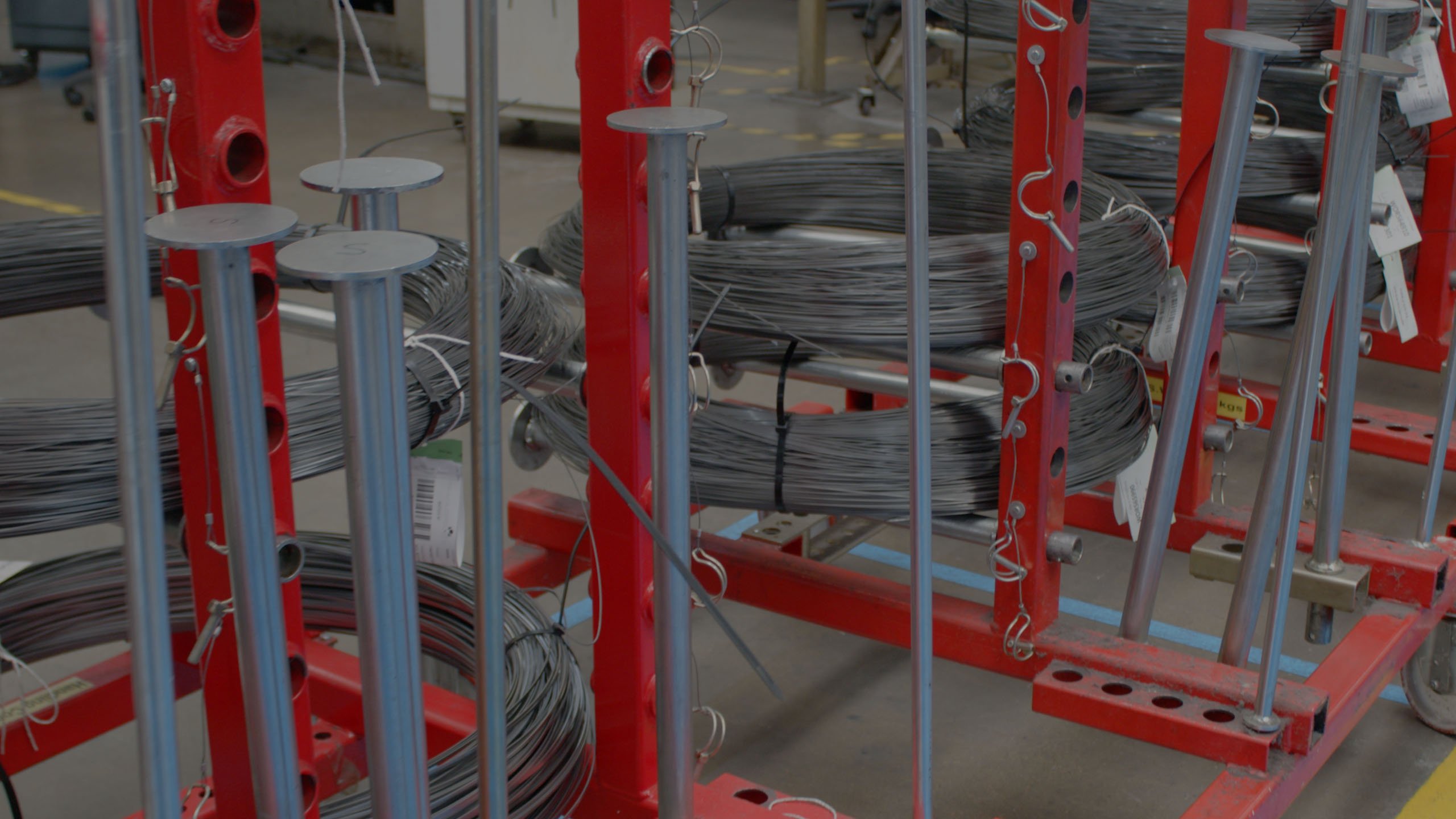 Coils of metal wire stored on red industrial racks in a manufacturing facility.