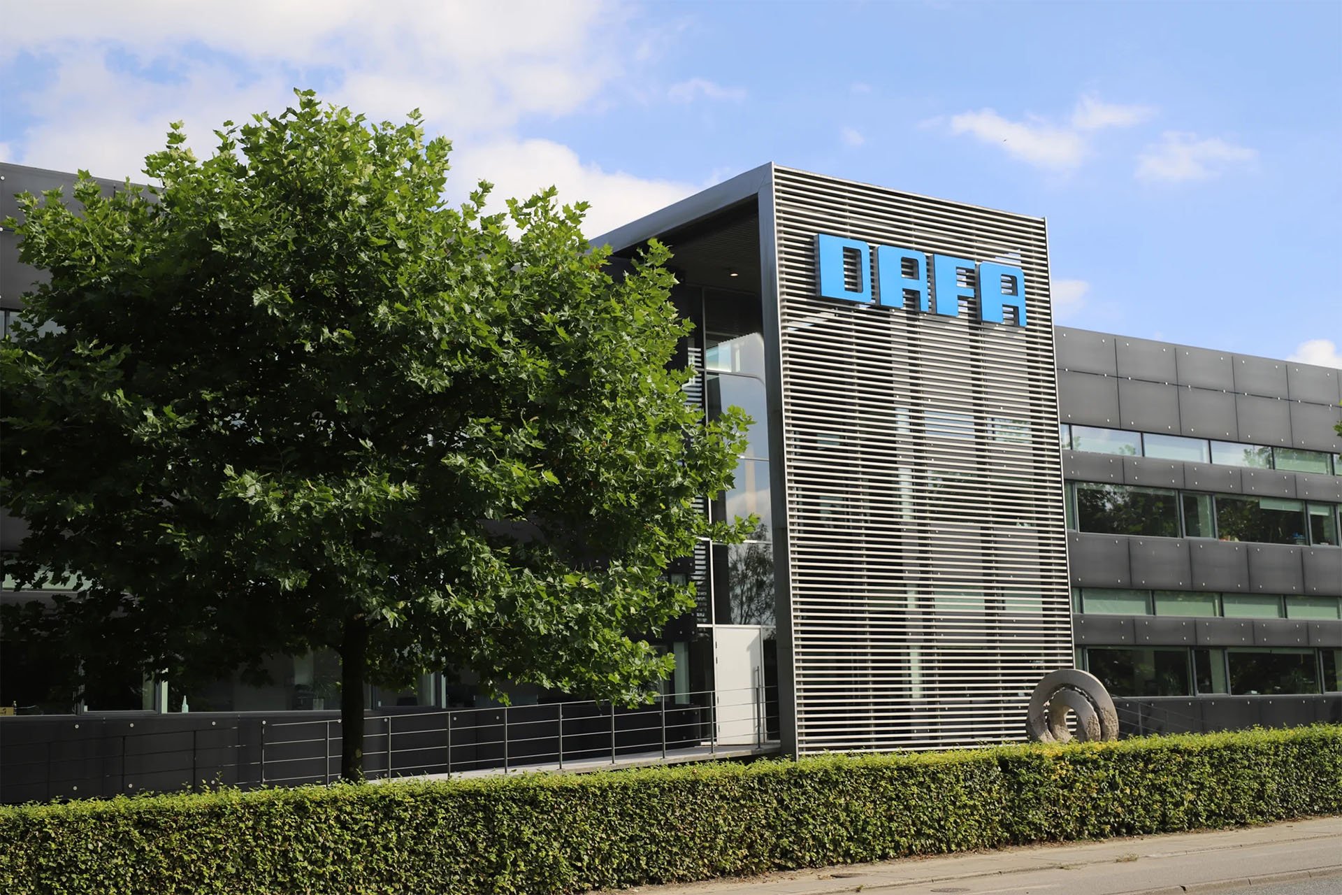 Modern office building with the DAFA logo on the facade, surrounded by greenery and a clear blue sky.