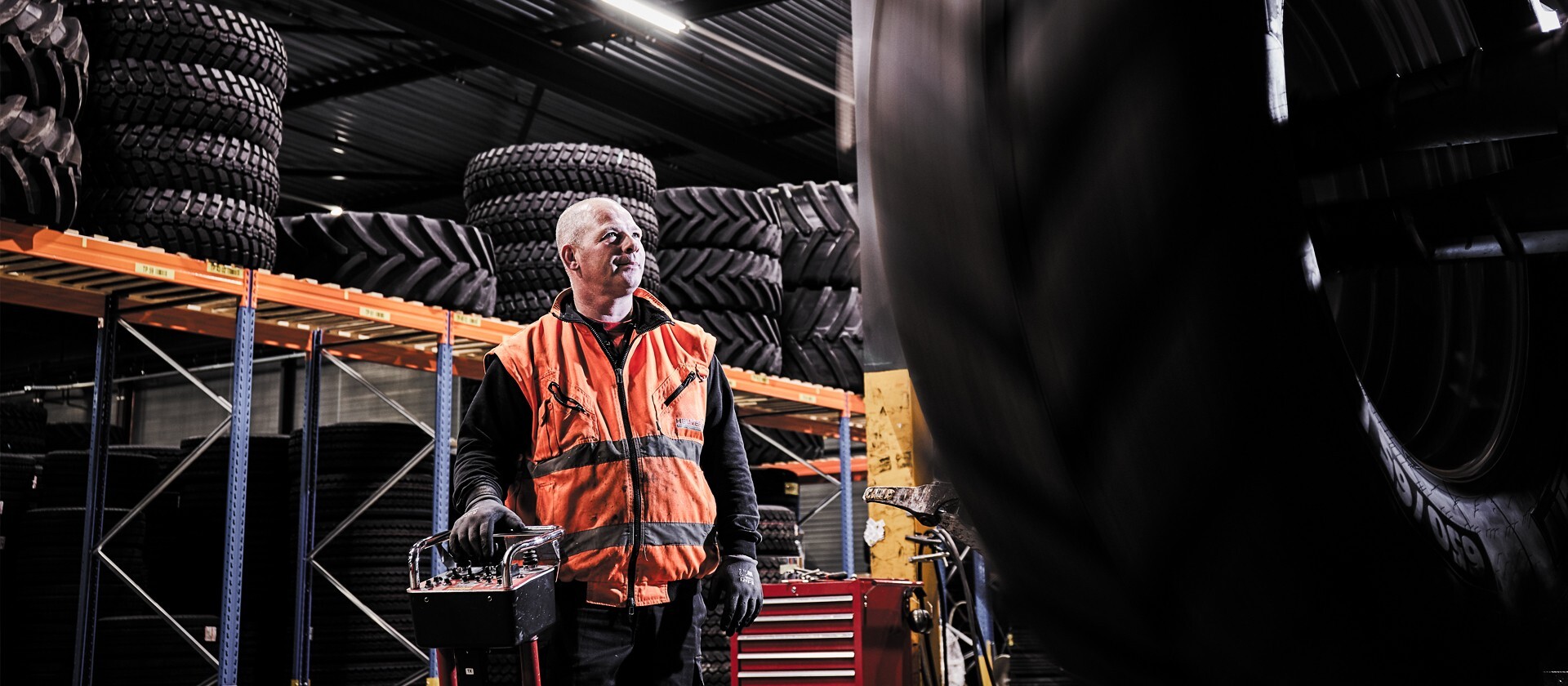Worker in safety vest operating equipment in a warehouse filled with large industrial tires.