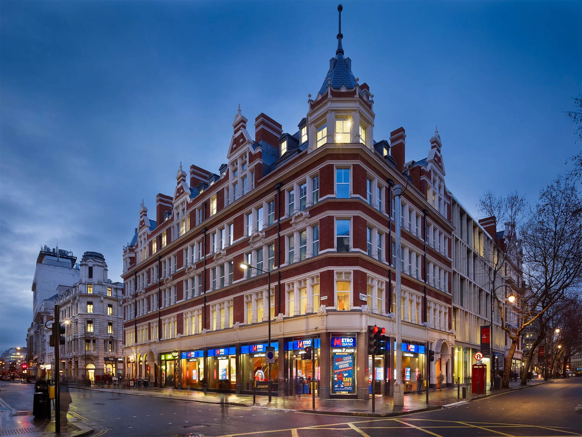 Corner view of a historic red-brick building housing Metro Bank in a city at dusk.