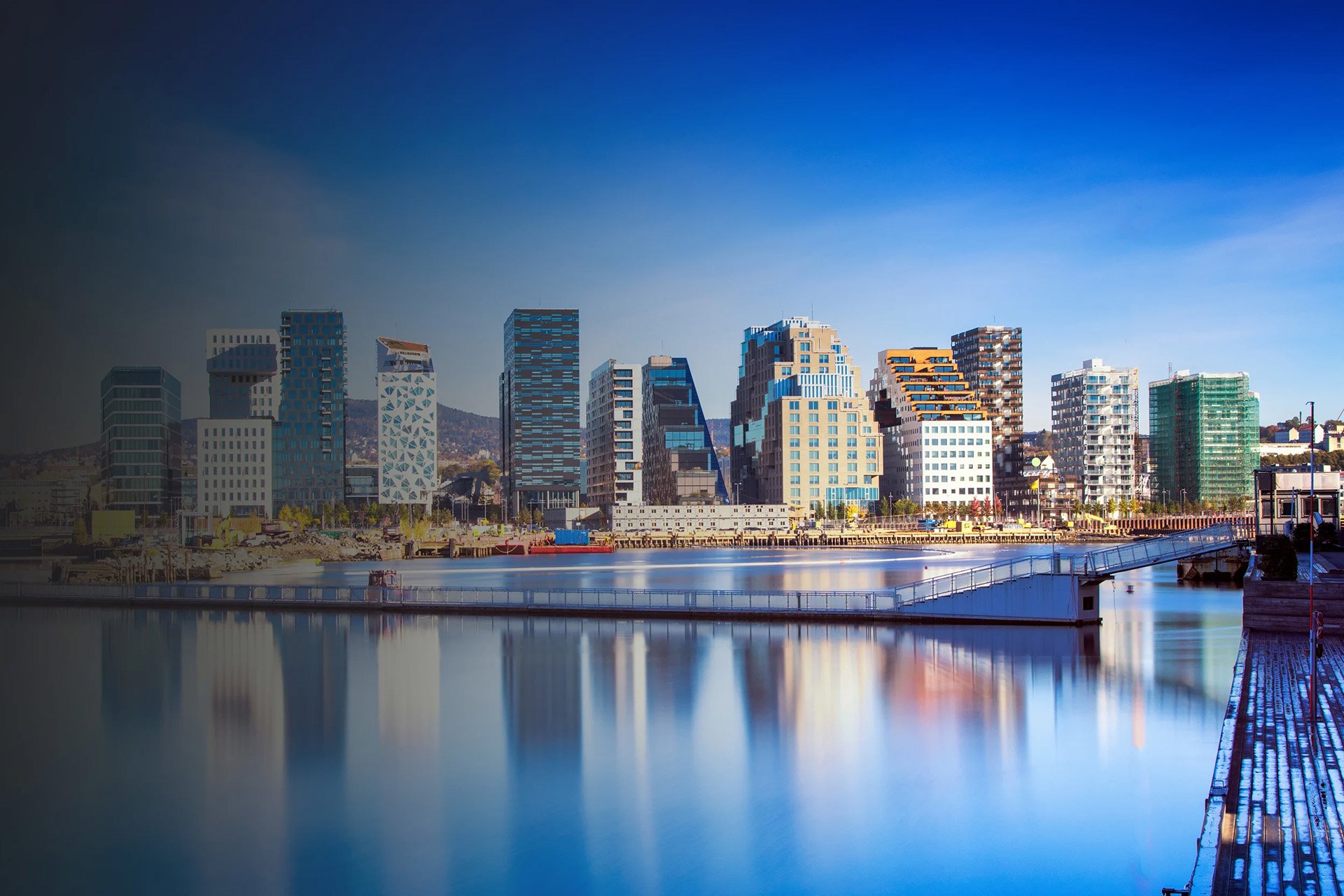 Modern city skyline reflected in calm water under a clear blue sky.