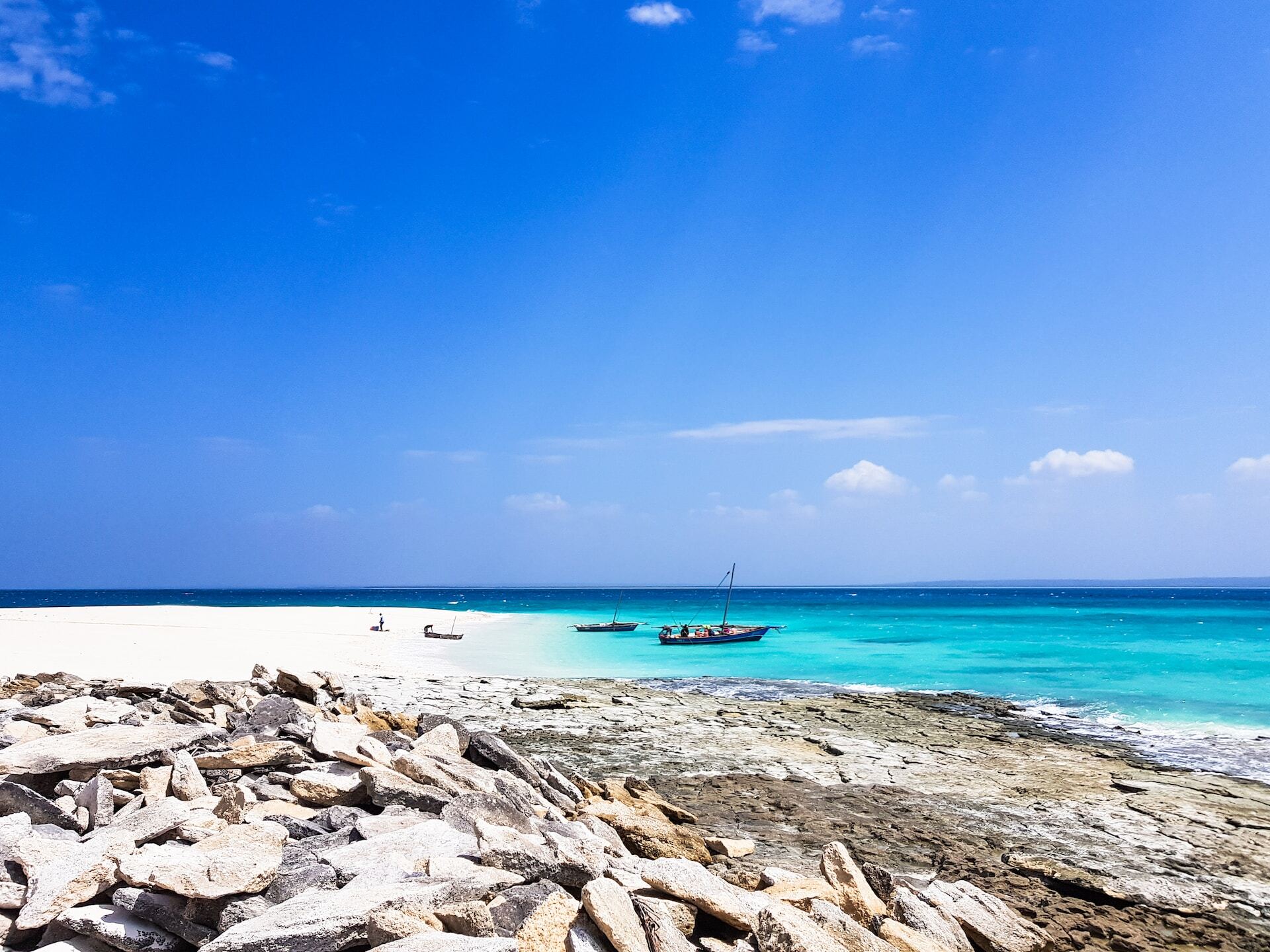 Scenic view of turquoise ocean, white sand beach, and traditional boats under a clear blue sky.