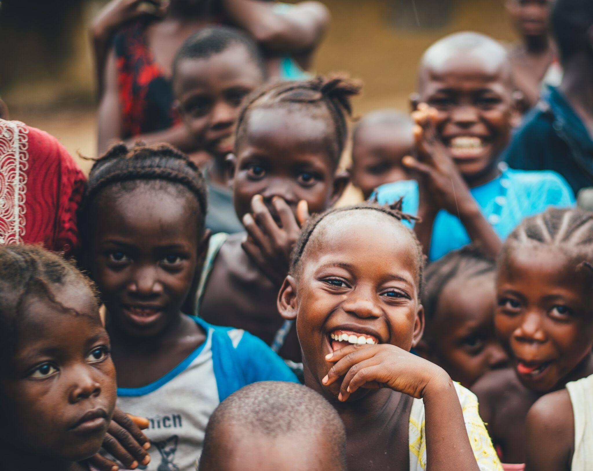 Group of smiling children gathered closely, looking at the camera.