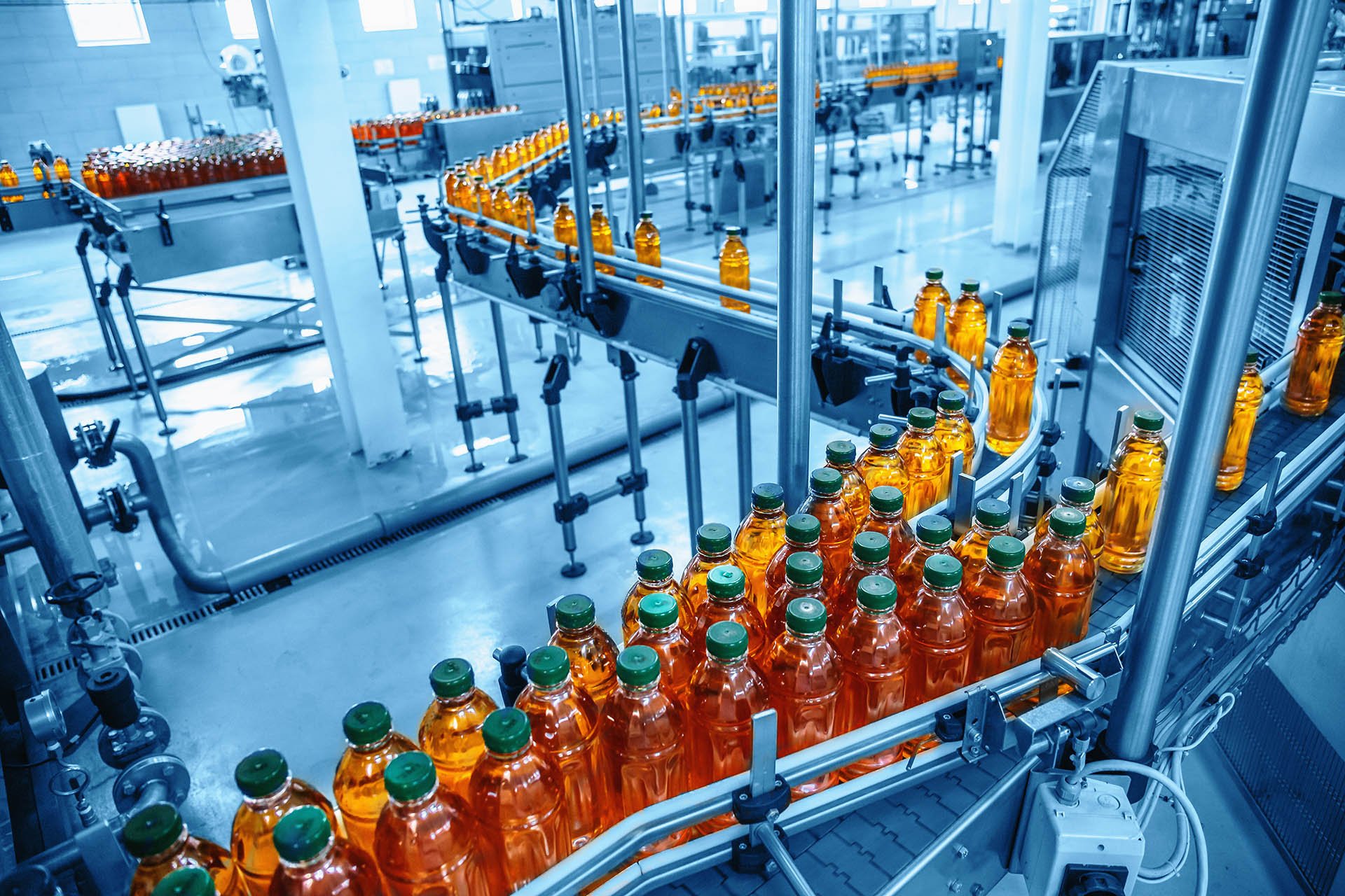 Ein Förderband in einer modernen Fabrik transportiert Reihen von Orangensaftflaschen mit grünen Verschlüssen. Die Umgebung ist sauber, effizient und industriell.