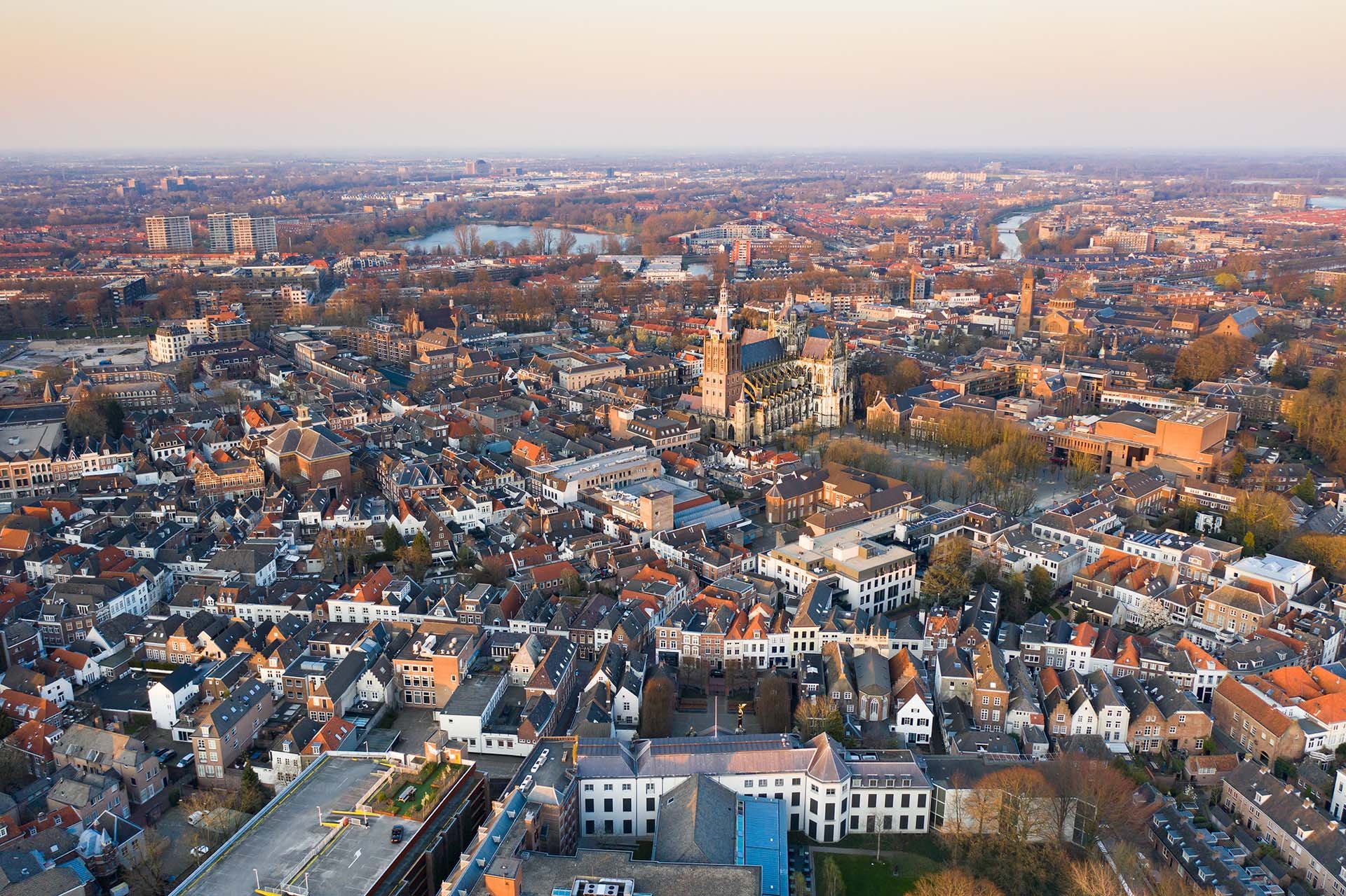 Aerial view of a European city at sunset, featuring historic architecture, winding streets, and a prominent church tower.