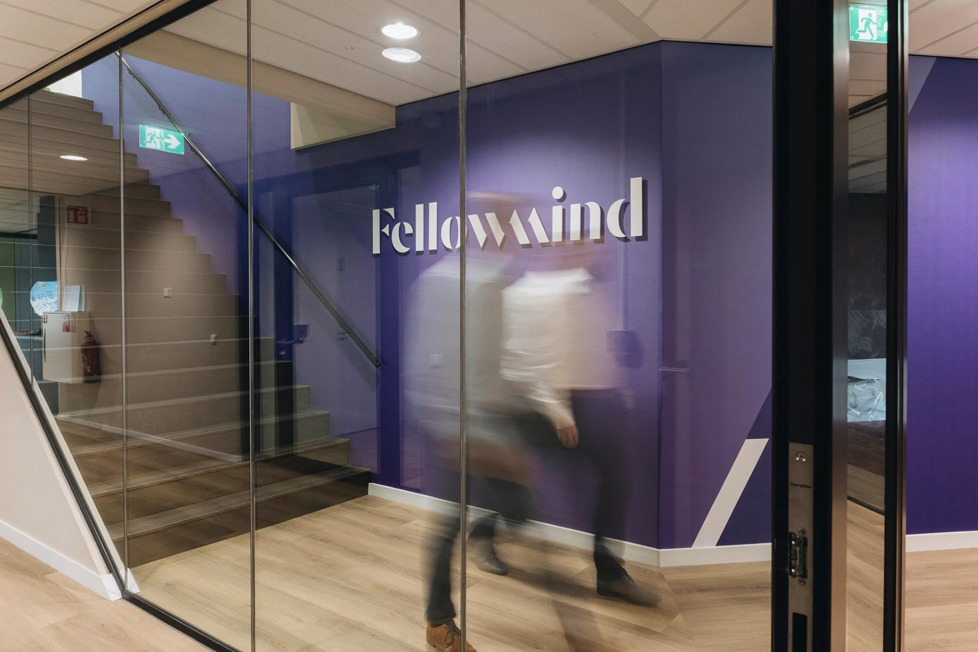 Two blurred figures walking past a glass wall, featuring the 