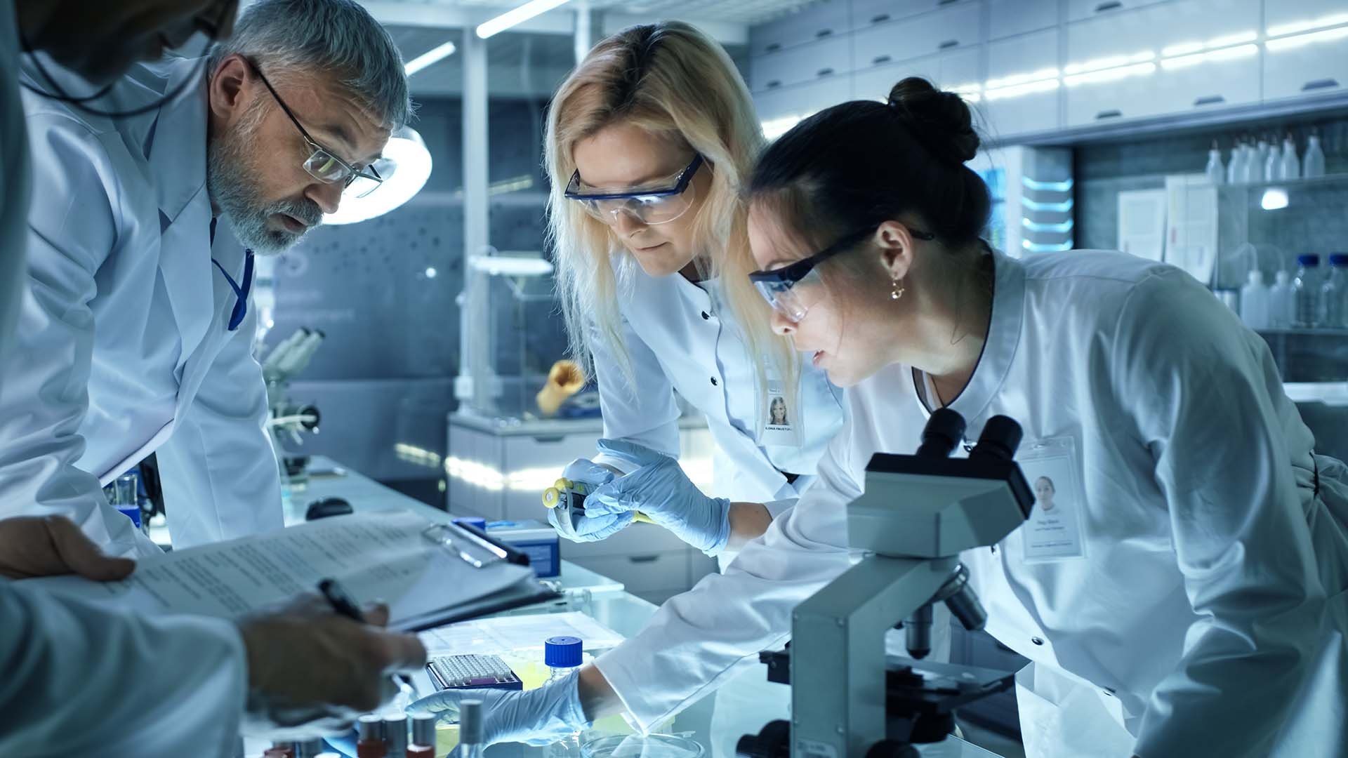 A group of scientists in lab coats examines samples and data at a modern laboratory equipped with advanced scientific tools.
