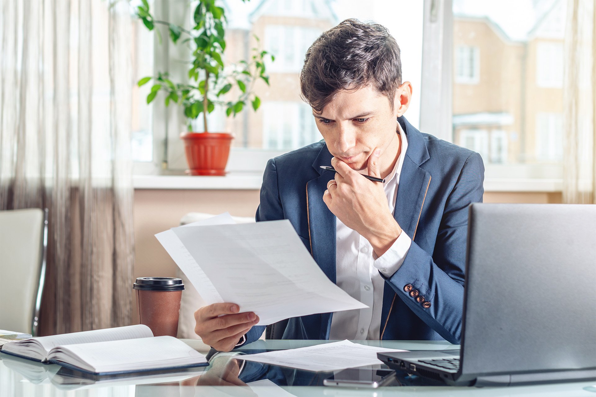 A man in a suit examines a document intently, focusing on the details on the paper.