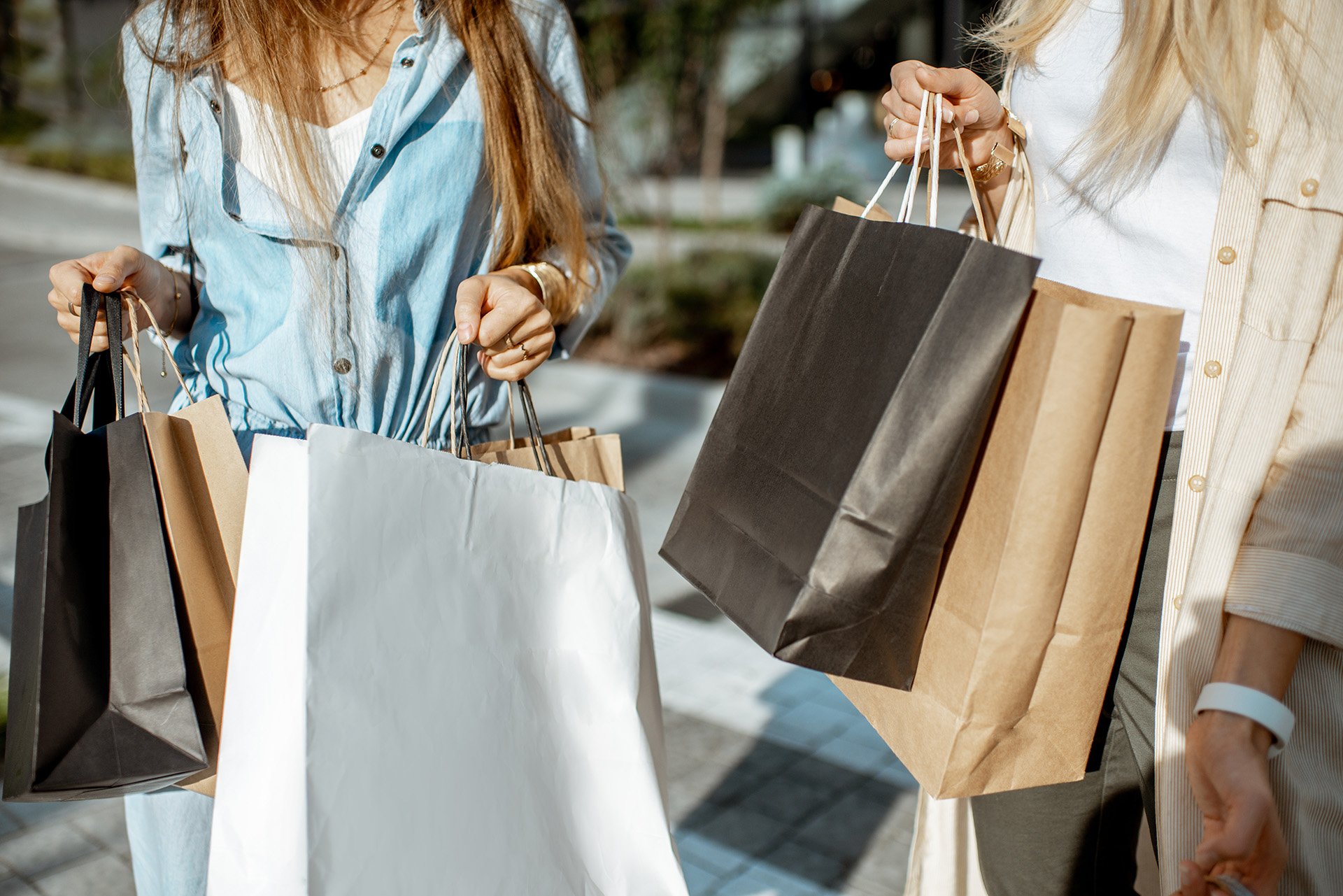 Two women smiling while holding shopping bags in a bustling city street.